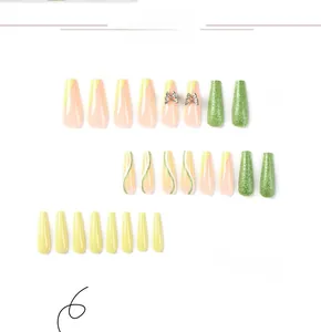 Detailed view of long coffin press-on nails with green French tips and 3D metal butterflies