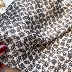 Detailed view of silky square scarf featuring geometric eye patterns in beige and brown