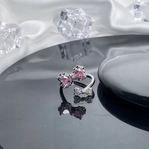 Close-up of silver bow ring with pink heart stones on a dark reflective surface