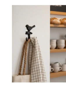 Detail eines Vintage-Vogelhakens aus Gusseisen an weißer Wand mit gewebter Tasche