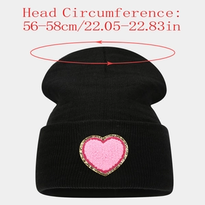 Detail of black knitted beanie with pink heart patch and gold shimmer embroidery