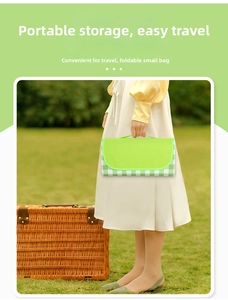 Foldable green checkered picnic mat with handle being carried outdoors by a model