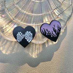 Detailed close-up of heart enamel pins with flame and skeleton hand motifs on shell tray