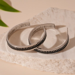 Detail of silver S925 hoop earrings with emerald-cut black stones on stone surface