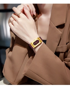 Close-up of rectangular gold watch with burgundy leather strap on woman's wrist