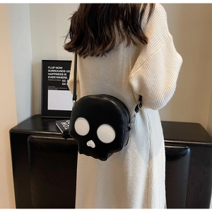 Black skull-shaped crossbody bag shown on a model wearing a beige sweater