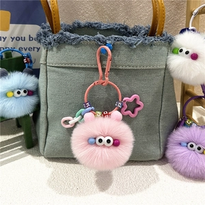 Pink plush charcoal ball keychain accessory on denim bag with soft fuzzy texture