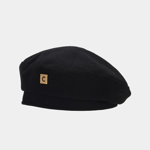 Close-up of black wool beret with a gold square metal C logo showing knit texture