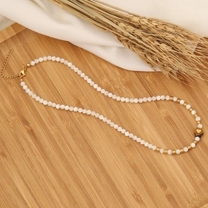 Detail of necklace with white shell pearls, gold beads and a heart pendant on wood