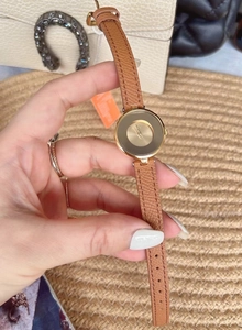 Close-up of minimalist women's watch with golden round dial and brown leather strap