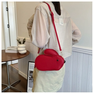 Détail du sac bandoulière rouge en forme de lapin sur un mannequin en intérieur