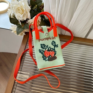 Detail of green knitted pumpkin crossbody bag on textured glass with white roses decoration