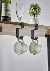 Macro detail of black metal under-shelf hook holding a cup on a wooden cabinet shelf