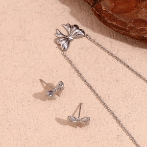 Detailed close-up of polished silver bow necklace and stud earrings set on a neutral base