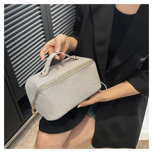 Detail showing grey textured cosmetic bag with gold zipper held by a hand