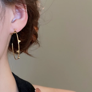 Detail of gold oversized hoop earring with triangular studs worn on ear lobe
