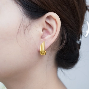 Close-up of gold irregular multi-layered J-shaped hoop earrings worn by a female model
