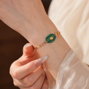 Détail d'un bracelet gourmette vintage doré avec breloques soleil et pierre malachite