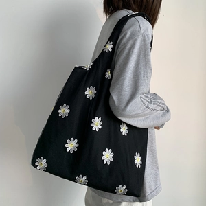 Detail of black canvas tote bag with white daisy embroidery on female model shoulder