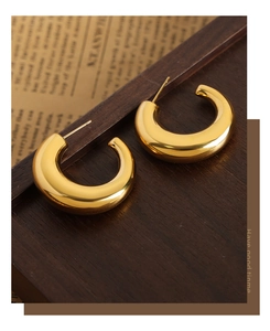 Detail of golden irregular C-shape earrings on vintage newspaper and wood background