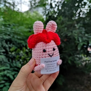 Makroaufnahme einer rosa Häkel-Hasenpuppe, die eine Motivationskarte in der Hand hält