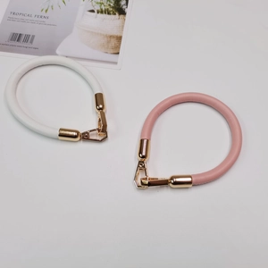 Detail of round leather bag handles in white and pink with golden spring buckles