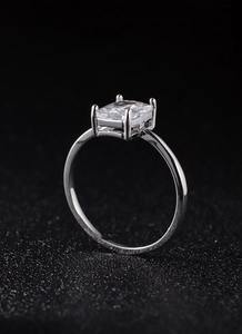 Macro shot of square clear zircon ring with silver four-prong setting on dark background