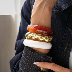 Detail showing stacked amber resin, gold twisted metal, and cream resin bangles