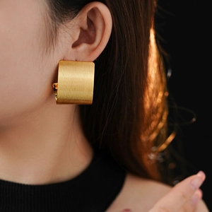 Detail of geometric brushed gold rectangular earrings worn by a model in warm light