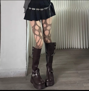 Detail of ripped spiderweb pattern stockings with chunky buckled boots and star chain