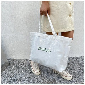 Detail of white PVC tote bag with Skillfully lettering held by model in minimalist setting