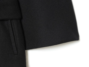 Close-up of black wool coat showing twill texture, cuff seams, and pocket stitch detail