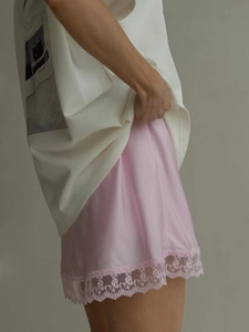 Close-up of pink satin skirt featuring delicate eyelash lace trim and glossy texture