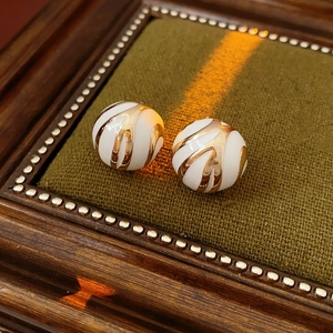 Macro shot of white sphere earrings with gold enamel swirls on a luxury velvet display box