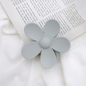 Detail of a large matte Morandi grey flower hair claw clip on vintage newspaper