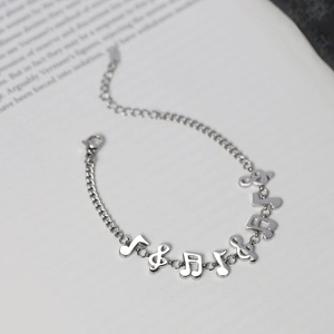 Detail showing musical note pendants on a silver titanium steel bracelet over book pages