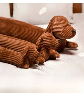 Détail de trois tailles de coussins en peluche teckel marron en velours côtelé sur lit