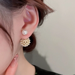 Close-up of gold plated pearl drop earrings with hollow sphere design on model