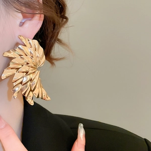 Detailed close-up of oversized gold pleated fan earrings with metallic leaf texture