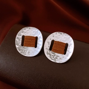 Detail of silver textured metal earrings with brown woven wrap on premium leather stand