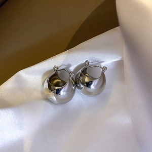 Detail view of silver spherical hoop earrings on glossy white silk fabric with soft focus