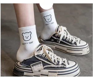 Detail of white cotton mid-calf socks with bear print and Happy Day text paired with shoes