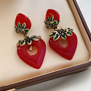 Vintage hollow red resin heart strawberry earrings with golden floral accents on velvet