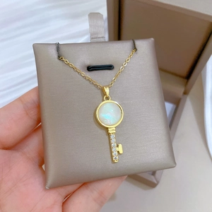 Macro view of gold key pendant necklace featuring a round opal and sparkling zircon inlay