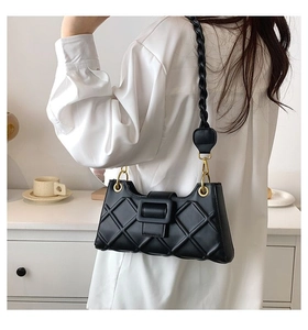 Detail of black quilted shoulder bag with textured strap on a person in a minimalist setting
