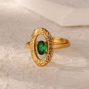 Dettaglio dell'anello dorato ovale con finitura martellata e gemma verde centrale
