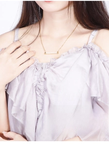 Détail d'un collier barre dorée avec micro-cristaux porté sur la clavicule d'une femme