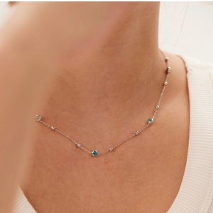 Detail of silver chain necklace with blue evil eye pendants worn by a model