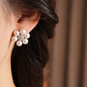 Close-up of a floral pearl earring with zircon center worn on a model's ear
