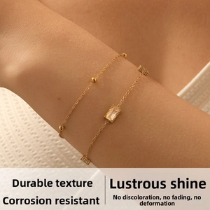 Detailed close-up of double-layer gold chain bracelet with beads and rectangular crystal